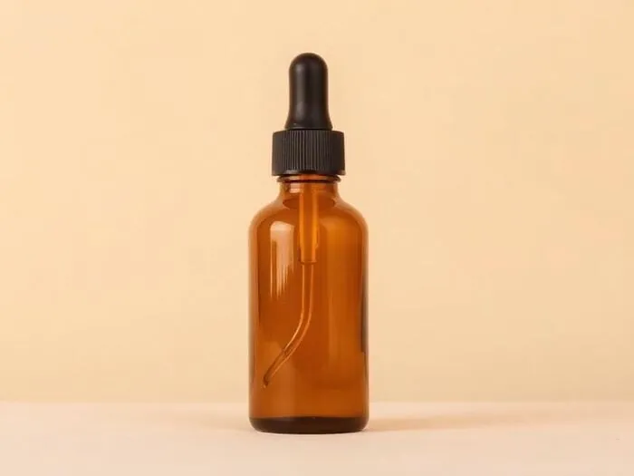 An amber glass skincare bottle with a dropper on a peach background.